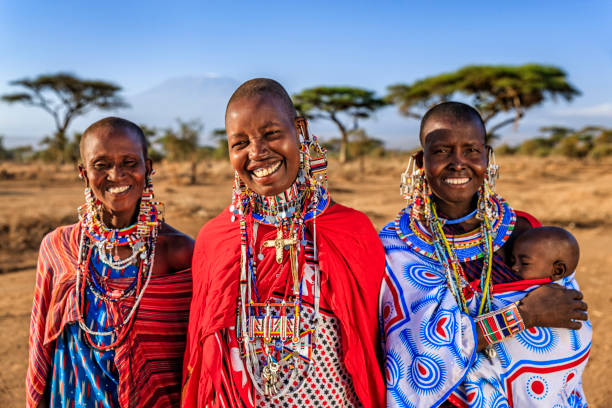Three Maasai women in traditional beadwork smiling, one holding her baby